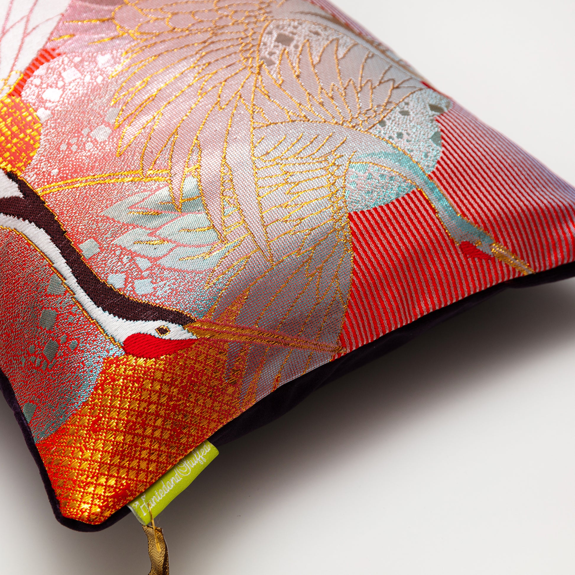 Photo of the edge of the pillow showing some cranes over eed silk on the front, a slight view of dark purple velvet back and the Hunted and Stuffed label.