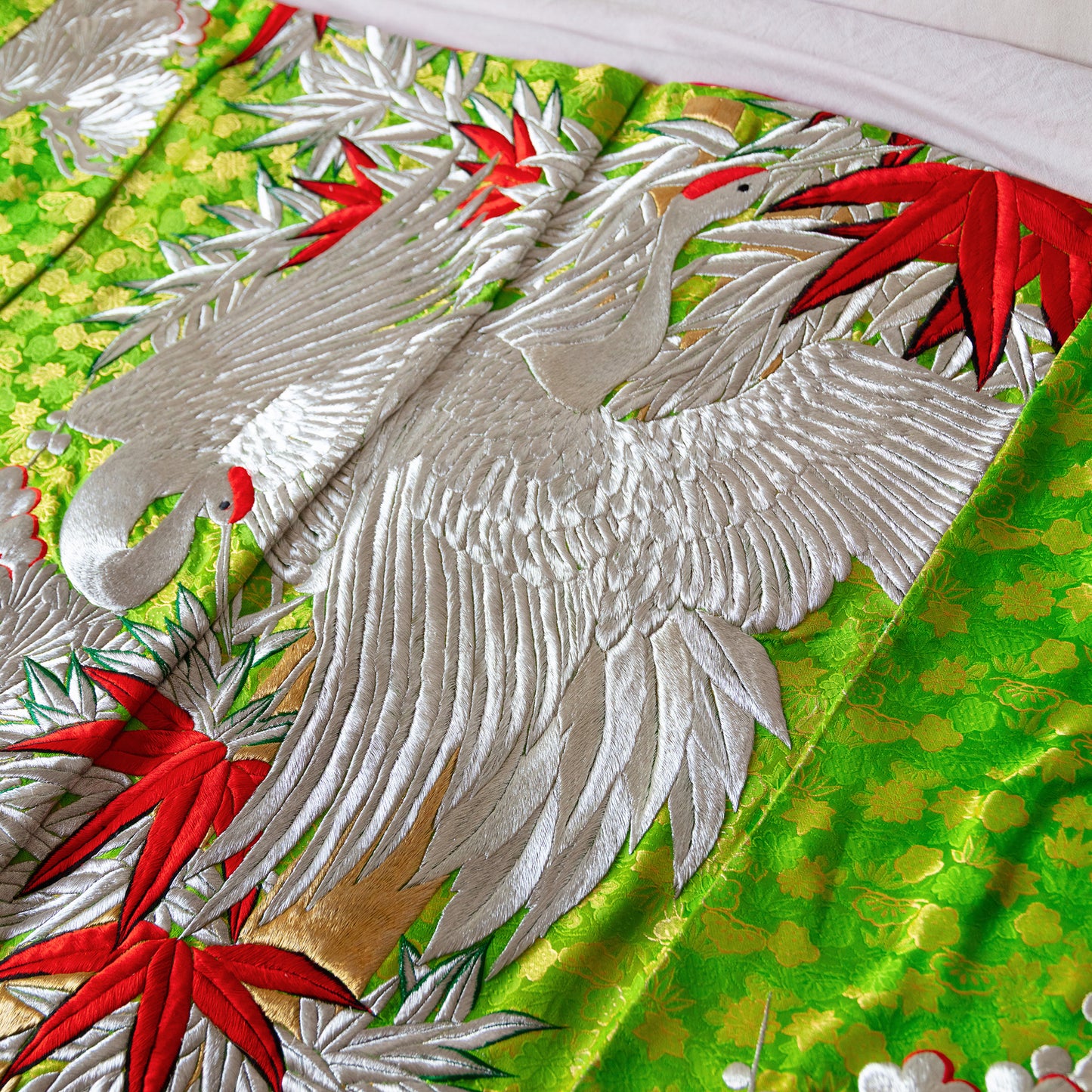 Detail of the green silk bedspread with silver crane birds and red leaf accents