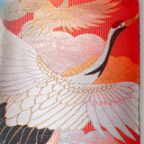 Close up detail of the pillow front, a flying crane with white silk wings over red background.