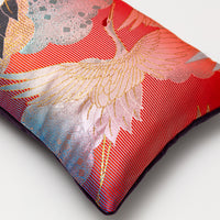 View of the other end of the pillow showing the gradient from blue to red in the silk base, there is a metallic flying crane woven over the top.