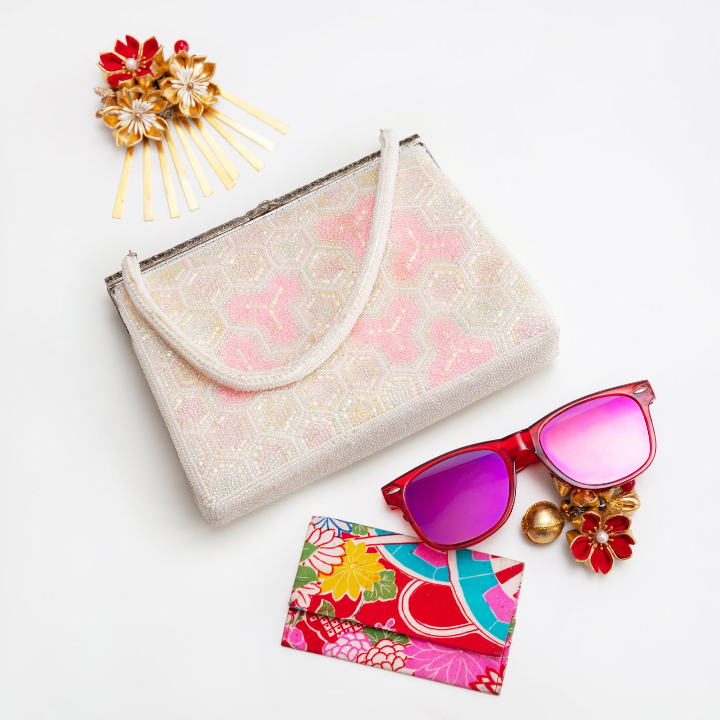 Geometric bead clutch bag, sunglasses with colouful case, and decorative hairpin on a white background