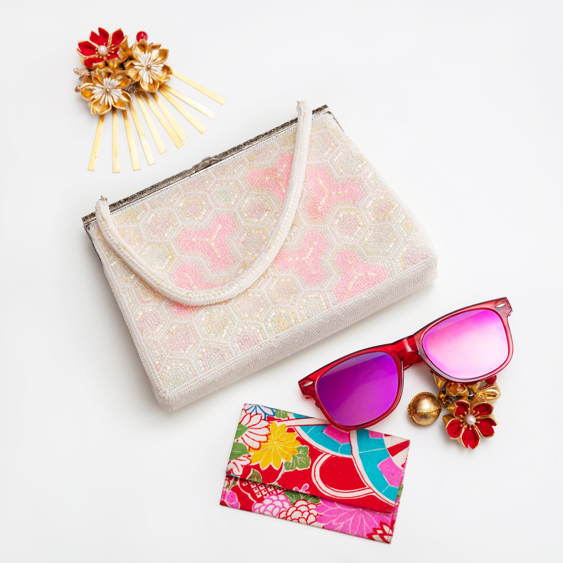 Geometric bead clutch bag, sunglasses with colouful case, and decorative hairpin on a white background