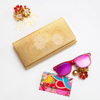 Close-up of gold metallic fabric with intricate floral kimono print and visible stitching detail on the foldover clutch edge.