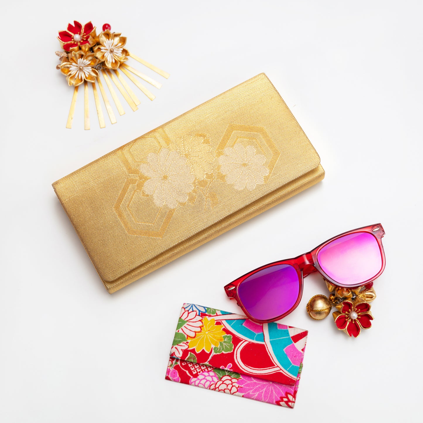 Vintage Japanese gold clutch with floral design, colorful sunglasses, and decorative hairpin on a white background