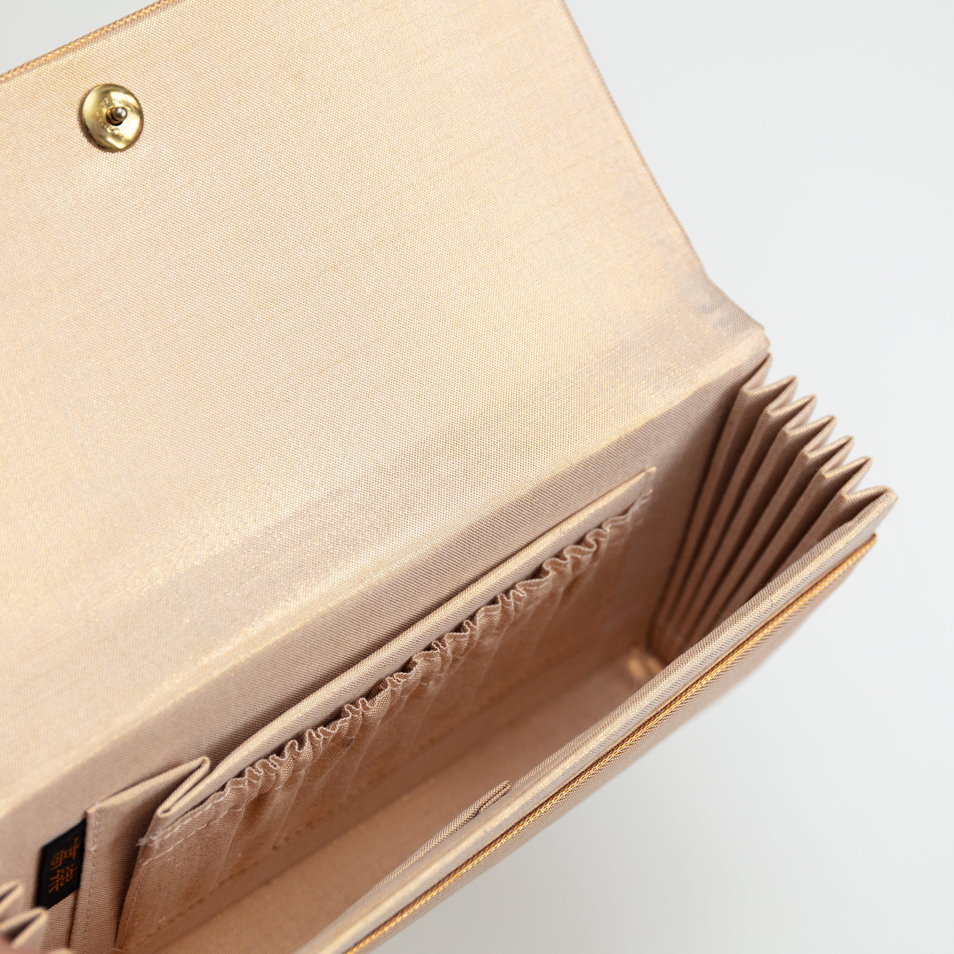 Detail of inside the gold envelope clutch with metallic gold and beige lining silk, internal pockets and gold metal closing stud on white background.