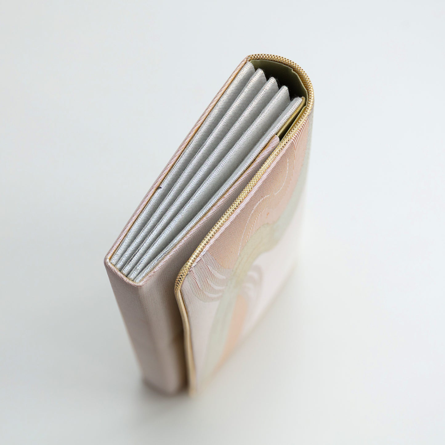 Close-up of a peach/pink metallic clutch bag with gold trim and silver side panels on a white background