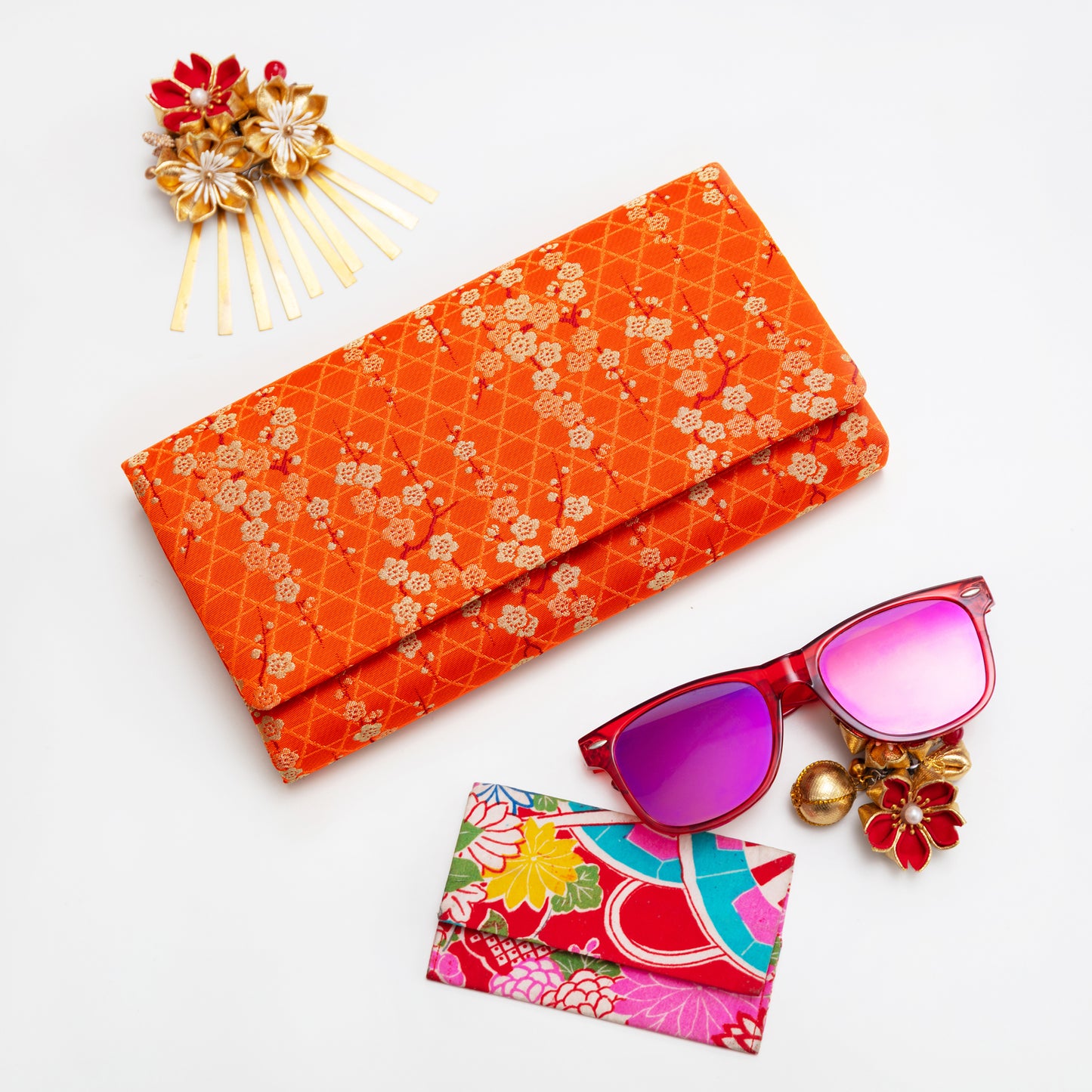 Orange floral clutch, pink sunglasses, colorful cardholder, and decorative hairpin on a white background