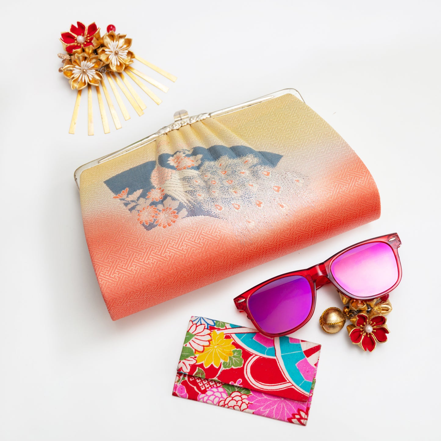 Colorful vintage Japanese silk clutch bag from the 1950s with floral, fan and peacock design, sunglasses with pink lenses, and decorative hairpin on a white background