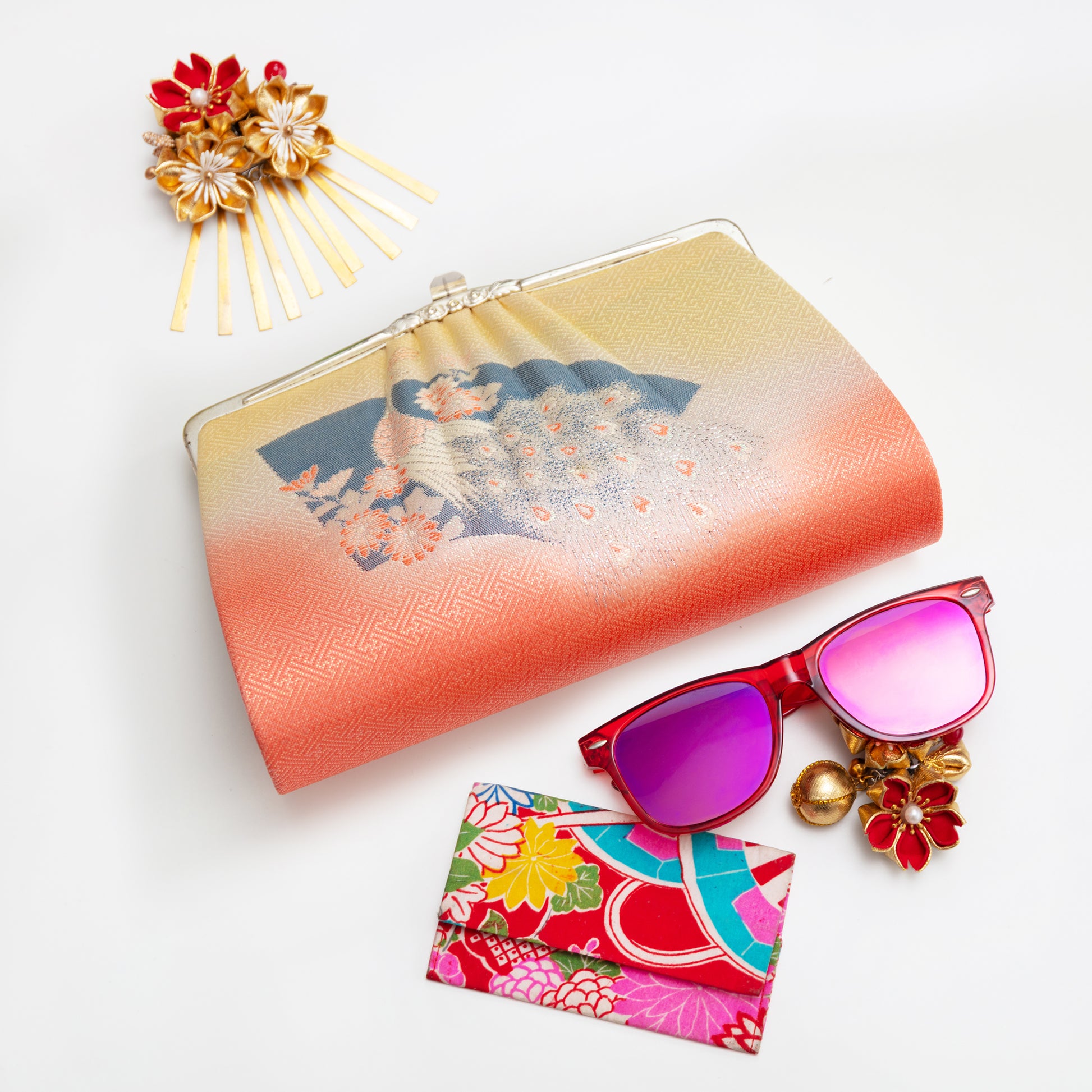 Colorful vintage Japanese silk clutch bag from the 1950s with floral, fan and peacock design, sunglasses with pink lenses, and decorative hairpin on a white background