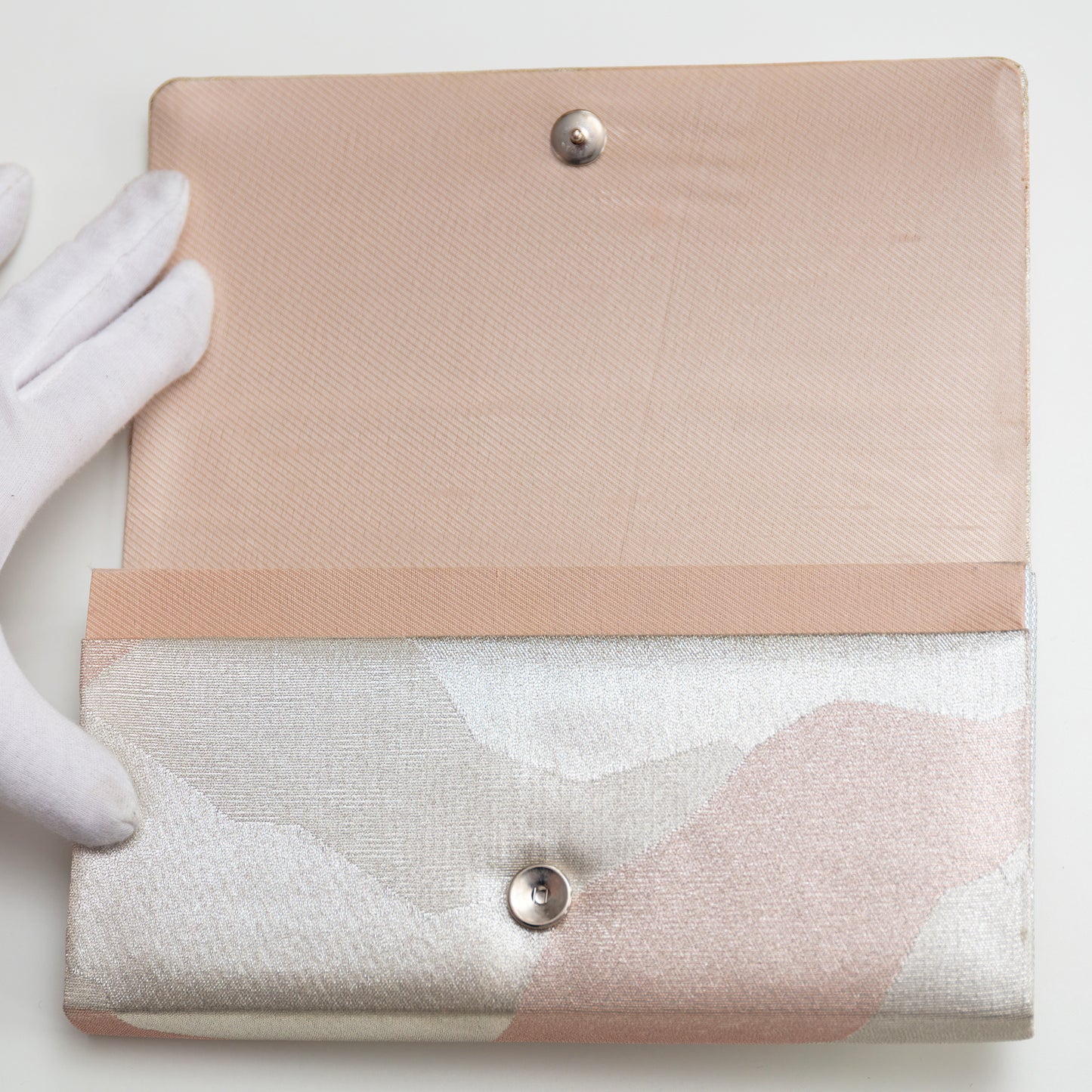 Silver and pink vintage Japanese clutch bag with pink silk lining being held open by a white gloved hand on a light background. Silver stud fastening.