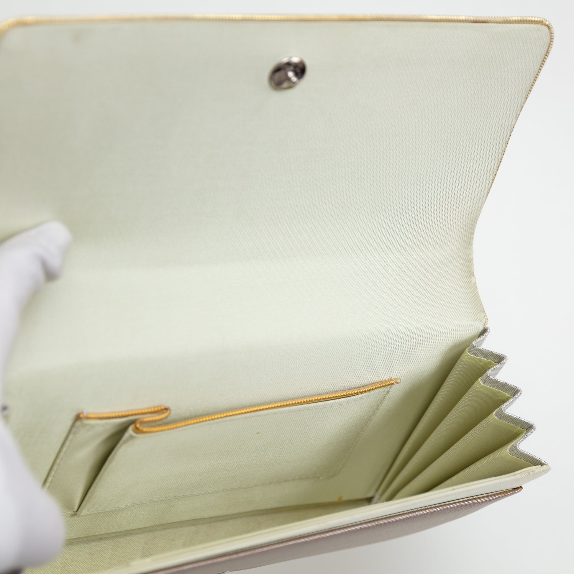 View inside the clutch bag with pale silk lining, gold trim on the internal pocket and the silver stud fastening on white background.