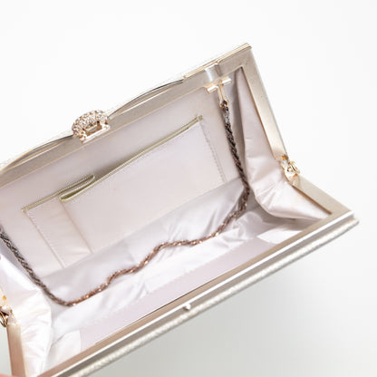 Close-up of a silver and white clutch with a decorative clasp on a light gray background. The strap hinges fold in to use the bag without the strap. Lined in white silk.