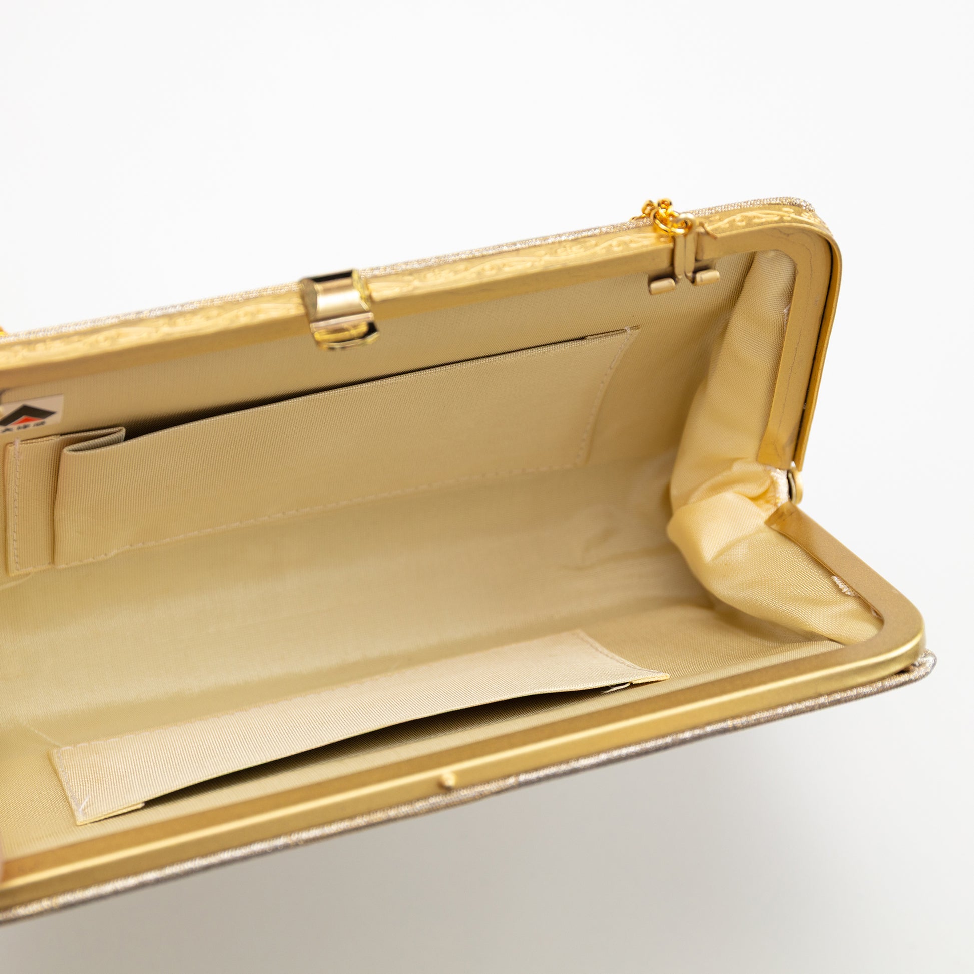 Gold clutch purse on a light gray background, convertible strap hinges and two internal pockets in cream silk.