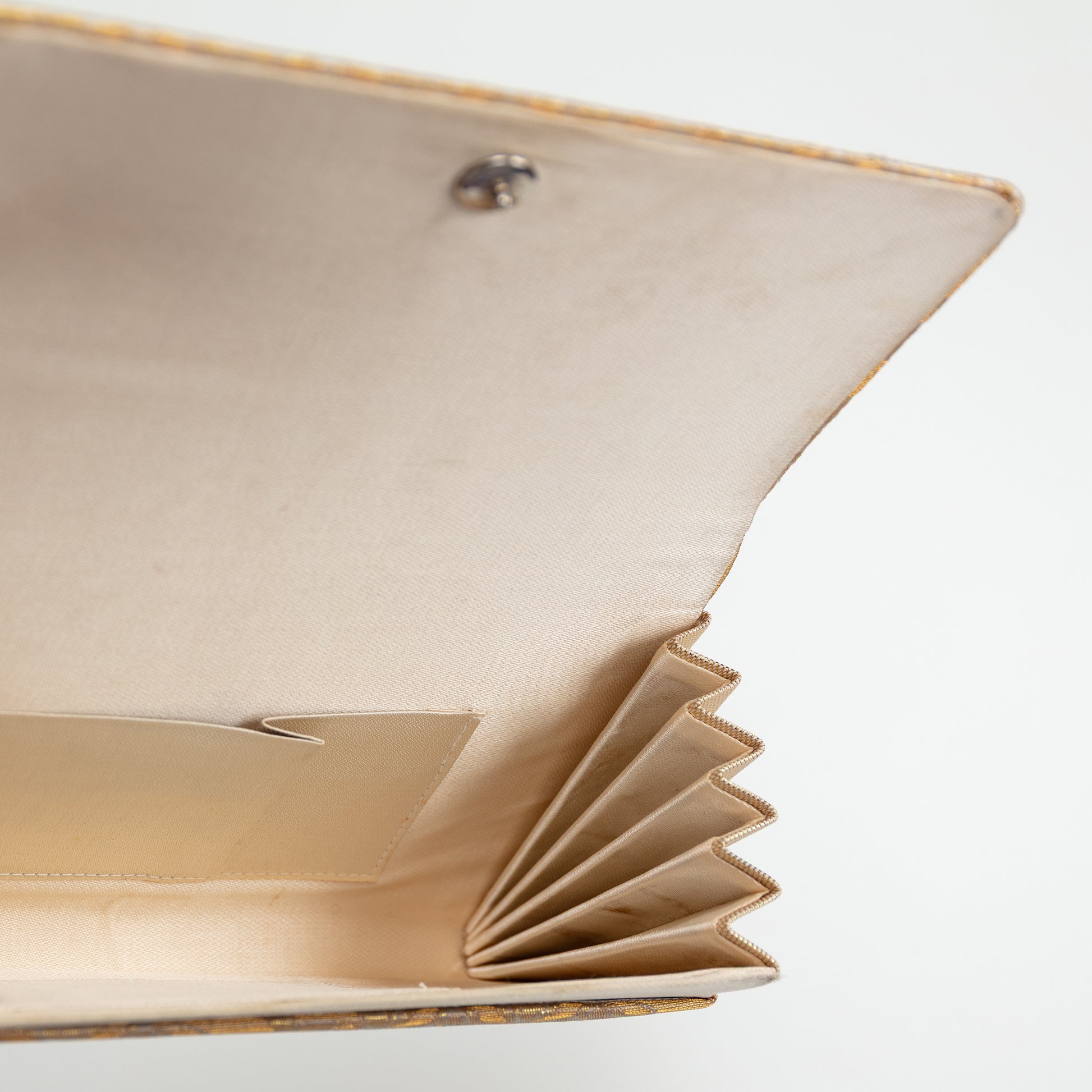 Detail of the open clutch bag interior showing internal pocket and metal stud fastener, gold trim to the edge, on white background.
