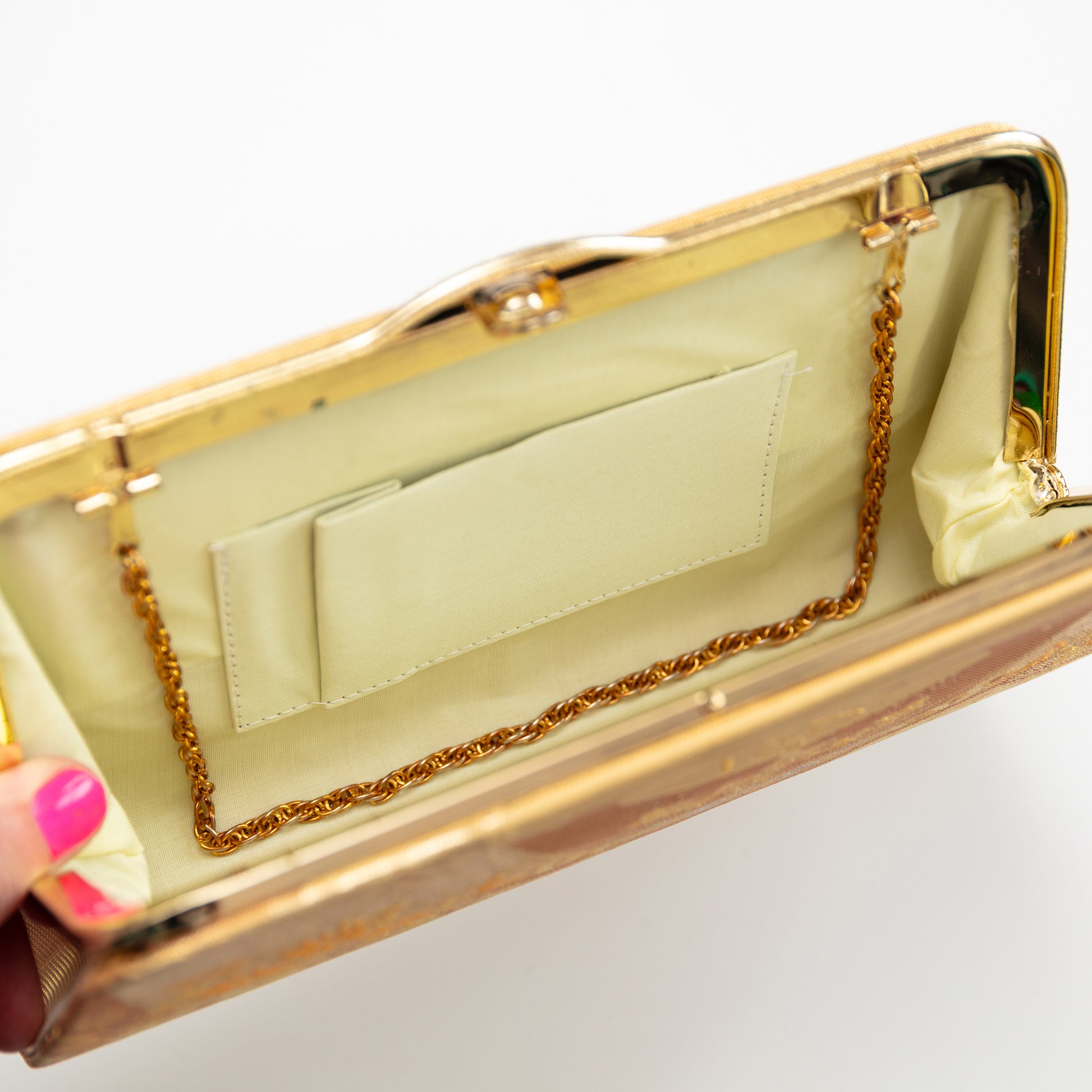 Gold clutch with a convertible chain strap on a white background