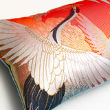 Detail of one end of the long bolster cushion showing an embroidered crane with wings open over a red, gold and blue woven silk background.