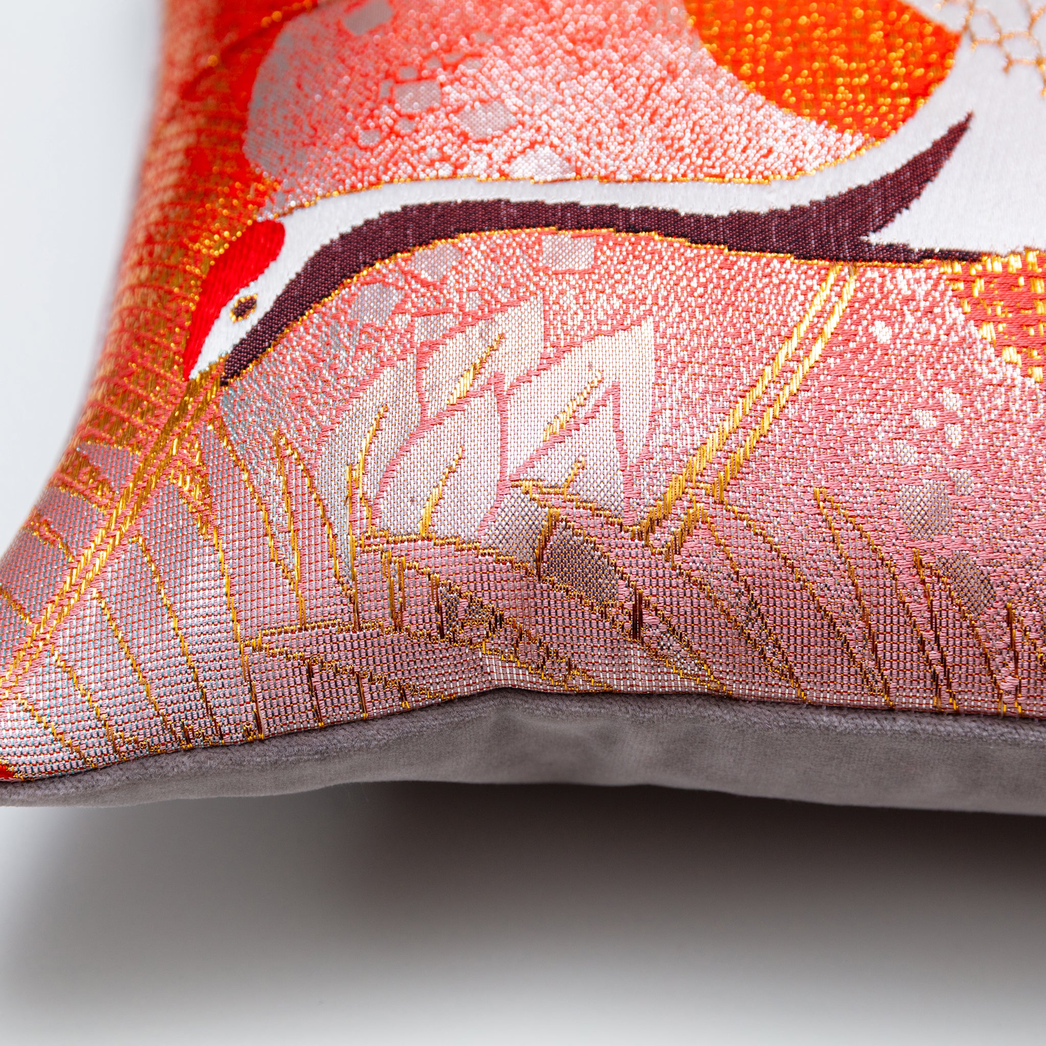 Close-up of the Rising Crane Peachy Red Silk pillow's textured silk surface with taupe velvet piping, showcasing intricate