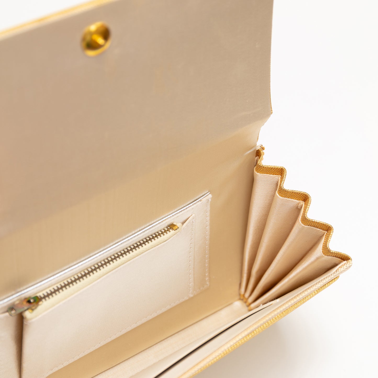 Close-up of a metallic gold handbag with beige silk lining and interior pockets on a white background