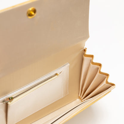 Close-up of a metallic gold handbag with beige silk lining and interior pockets on a white background