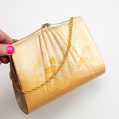 Vintage Japanese silk gold clutch bag with floral embroidery held by a hand on a white background