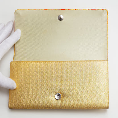 Gold clutch with textured surface and silver buttons held by a white-gloved hand on a light background