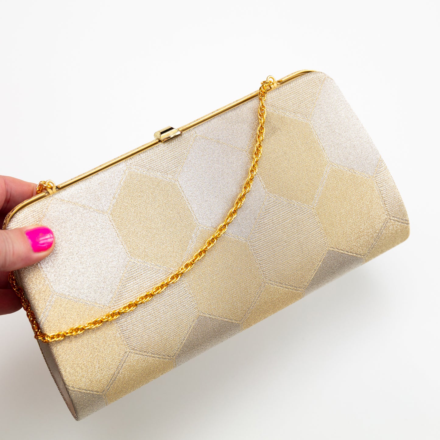 Metallic gold vintage Japanese clutch bag with gold chain held by a hand on a white background