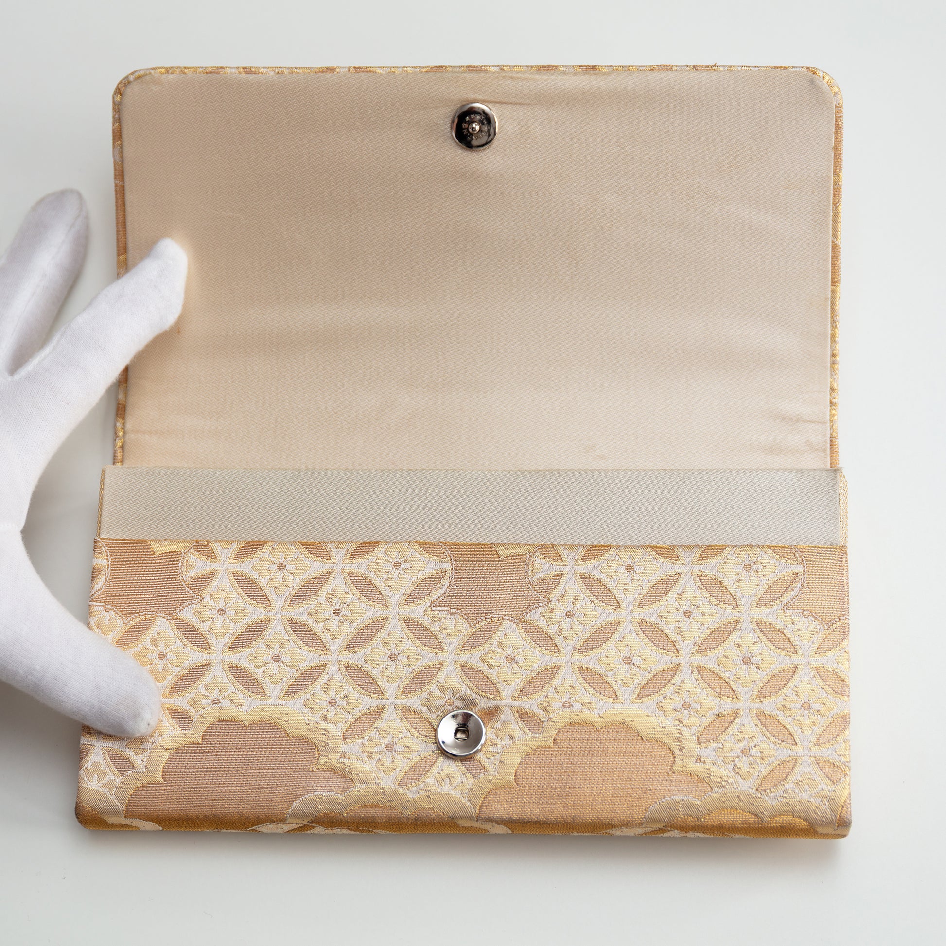 Interior view of the open envelope clutch bag with beige silk lining and stud fastening on a white background.