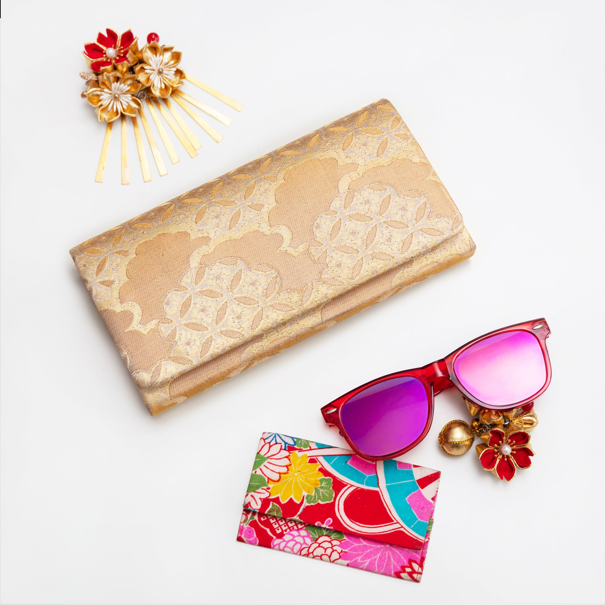 Gold clutch, pink sunglasses, colorful pouch, and decorative hairpin on a white background