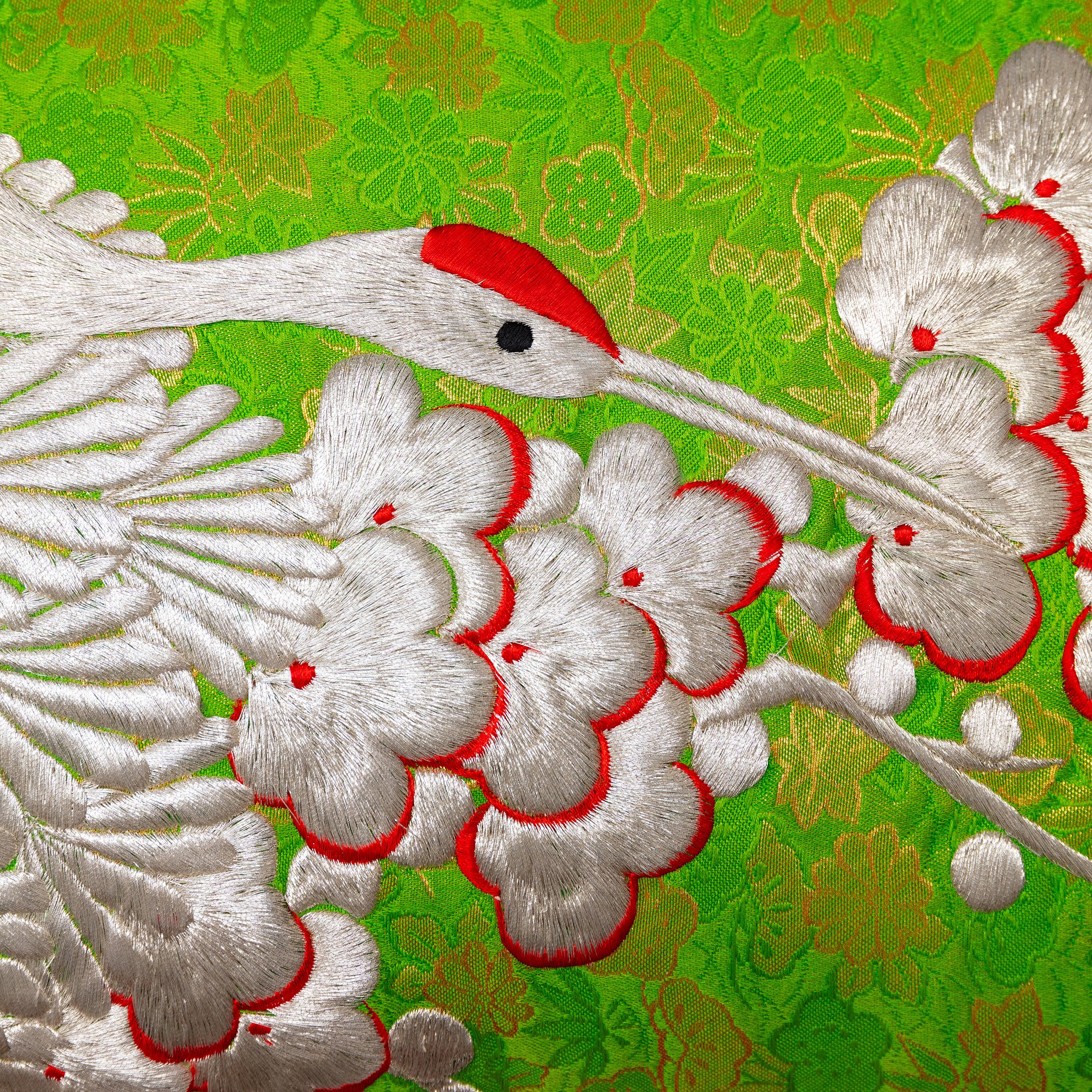Close-up of textured silk fabric highlighting intricate silver crane embroidery on the green bolster cushion.