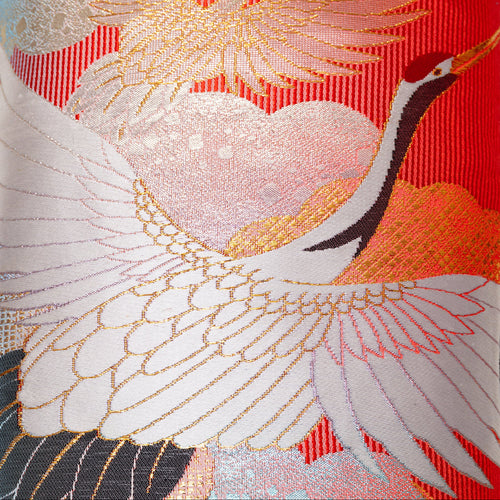 Close-up of rich red silk fabric highlighting intricate crane embroidery and subtle velvet sheen detail