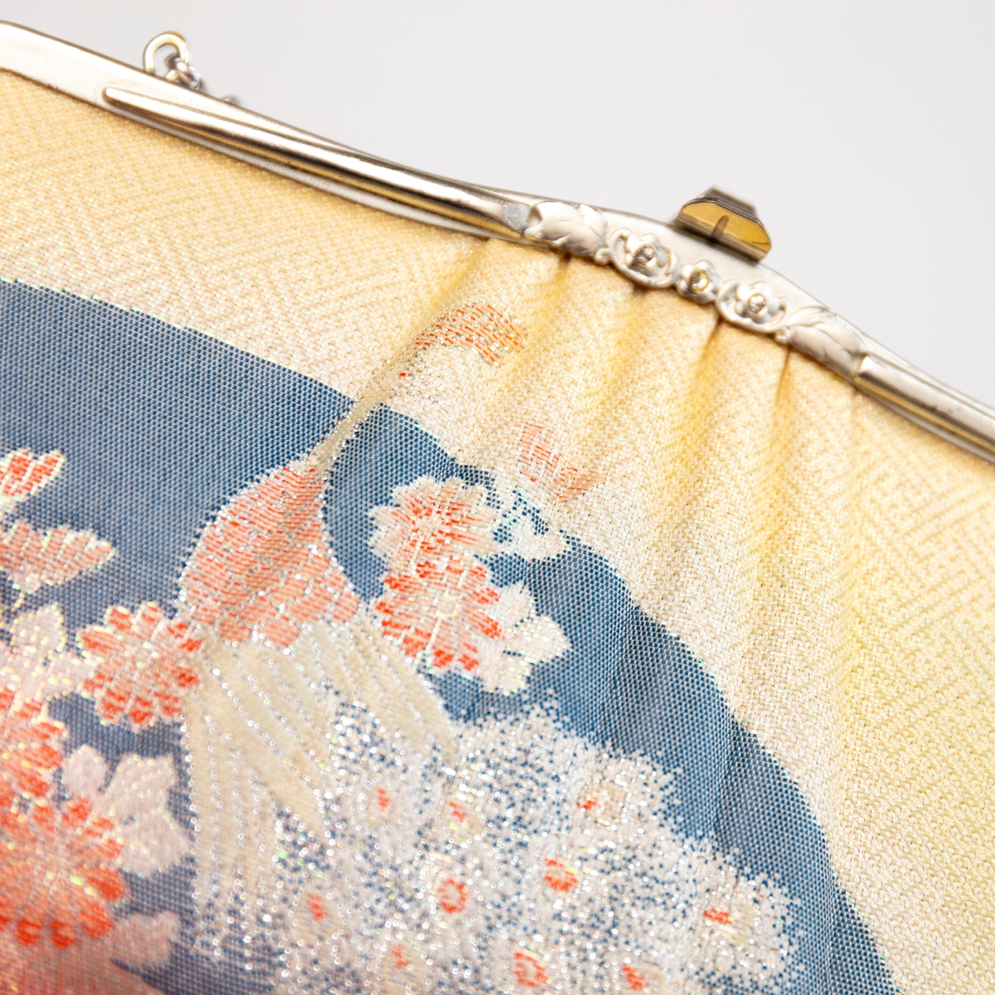 Close-up of a handbag with floral embroidery on a light background. Diamanté stones set into the frame. Peacock woven design.