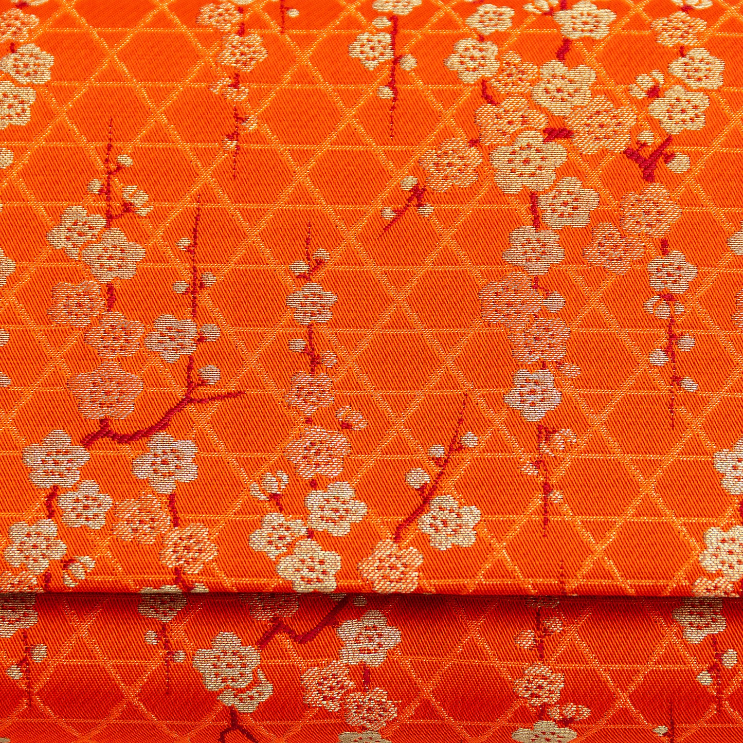 Orange silk with gold floral pattern of plum blossom and geometric lines. Close up of the front of the vintage 1970s orange silk clutch bag.