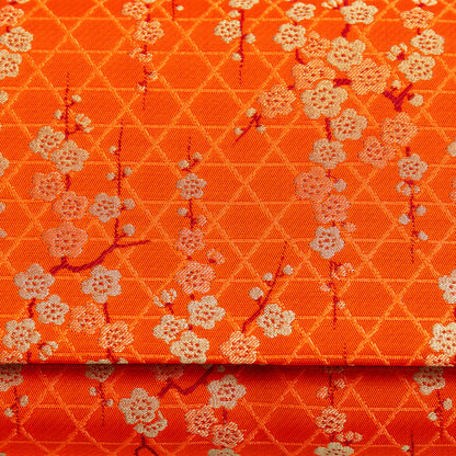 Orange silk with gold floral pattern of plum blossom and geometric lines. Close up of the front of the vintage 1970s orange silk clutch bag.