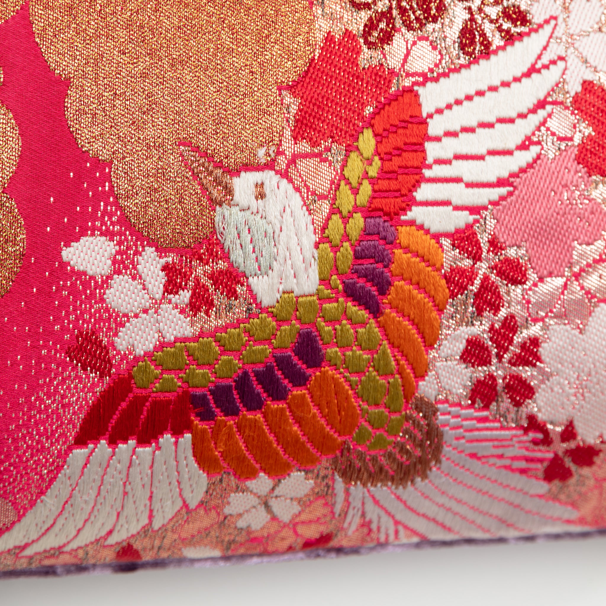 Close-up of vibrant red gold cranes and lilac velvet fabric highlighting intricate embroidery details and rich textures