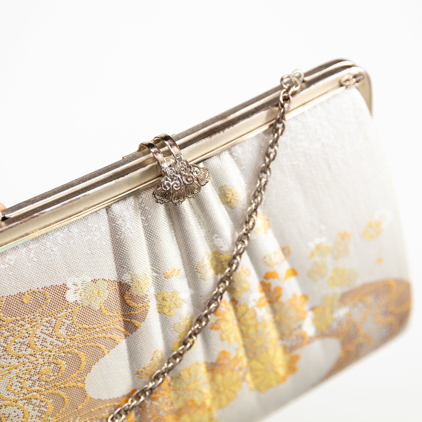 White clutch bag with gold floral pattern and chain strap on a white background