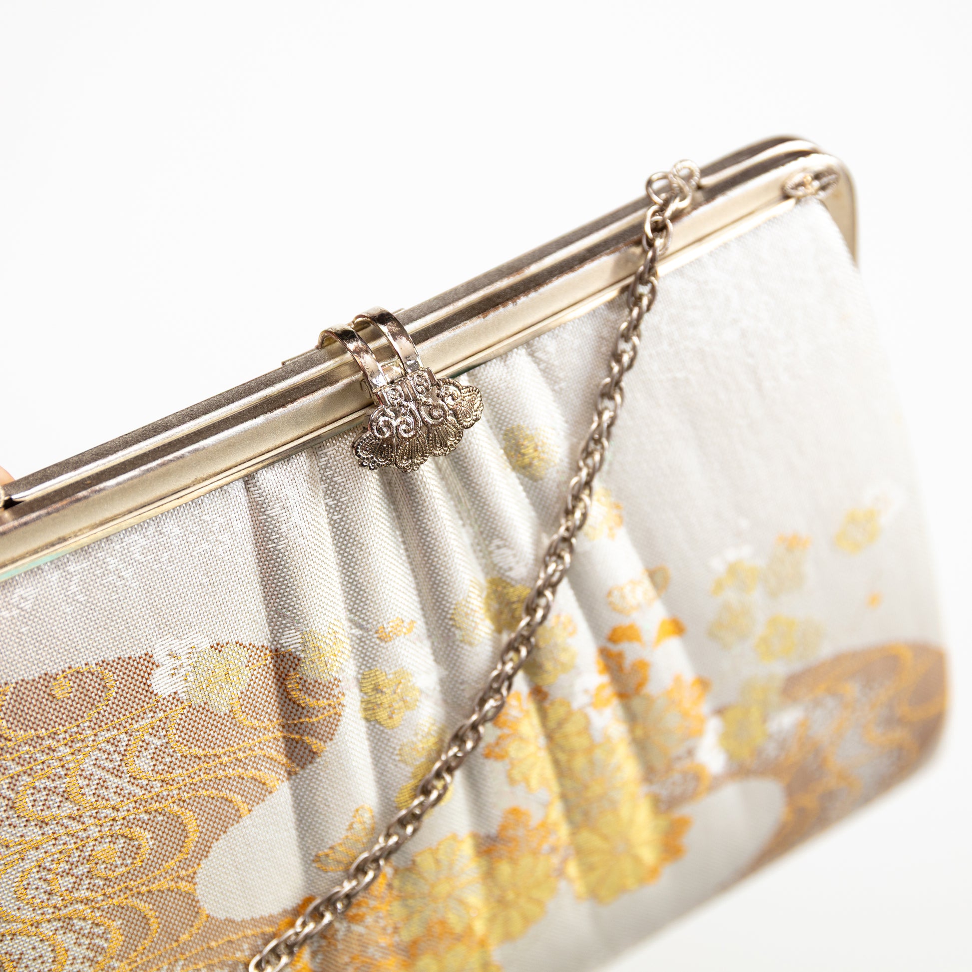 White clutch bag with gold floral pattern and chain strap on a white background
