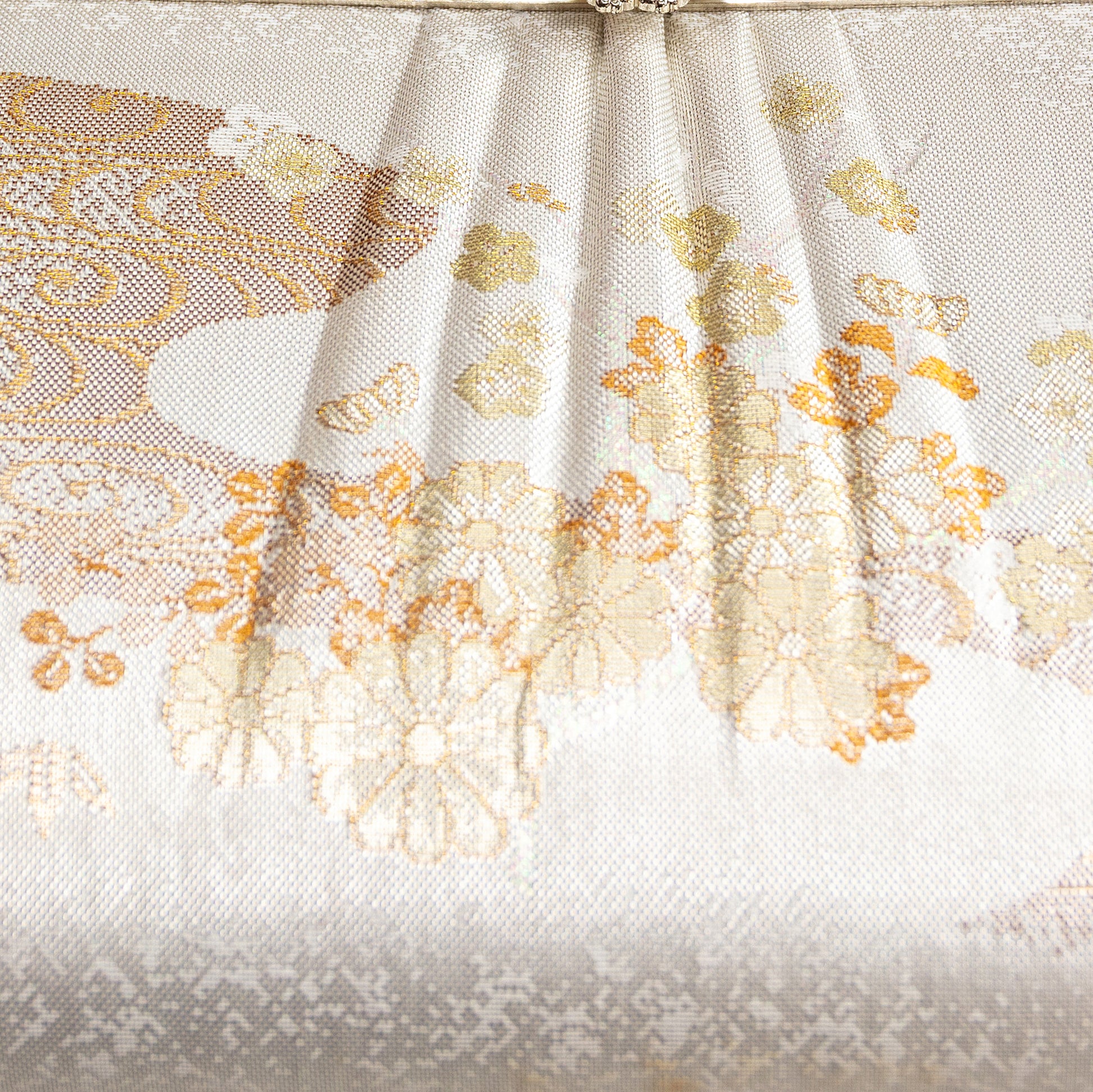 Close-up of a woven kimono silk fabric with floral patterns on a white background. Detail of the clutch bag front.