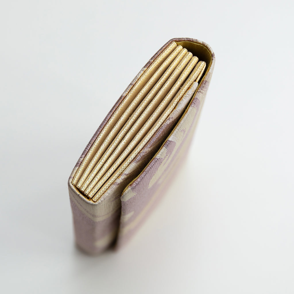 Close-up of the lilac silk clutch’s woven envelope flap showing delicate texture and subtle wave pattern detail.