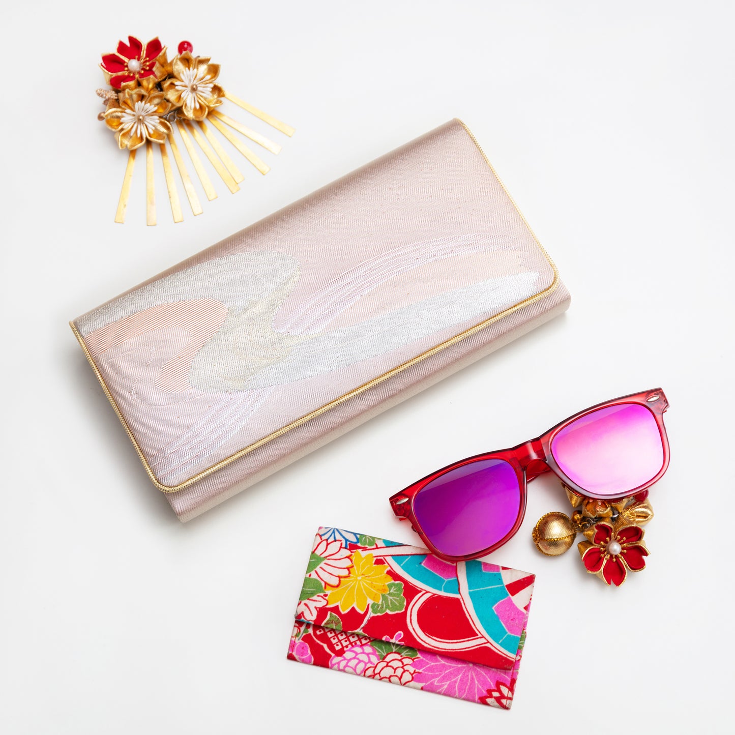 Pink vintage kimono silk wallet, with gold trim, sunglasses with pink lenses, floral cardholder, and decorative hairpin on a white background