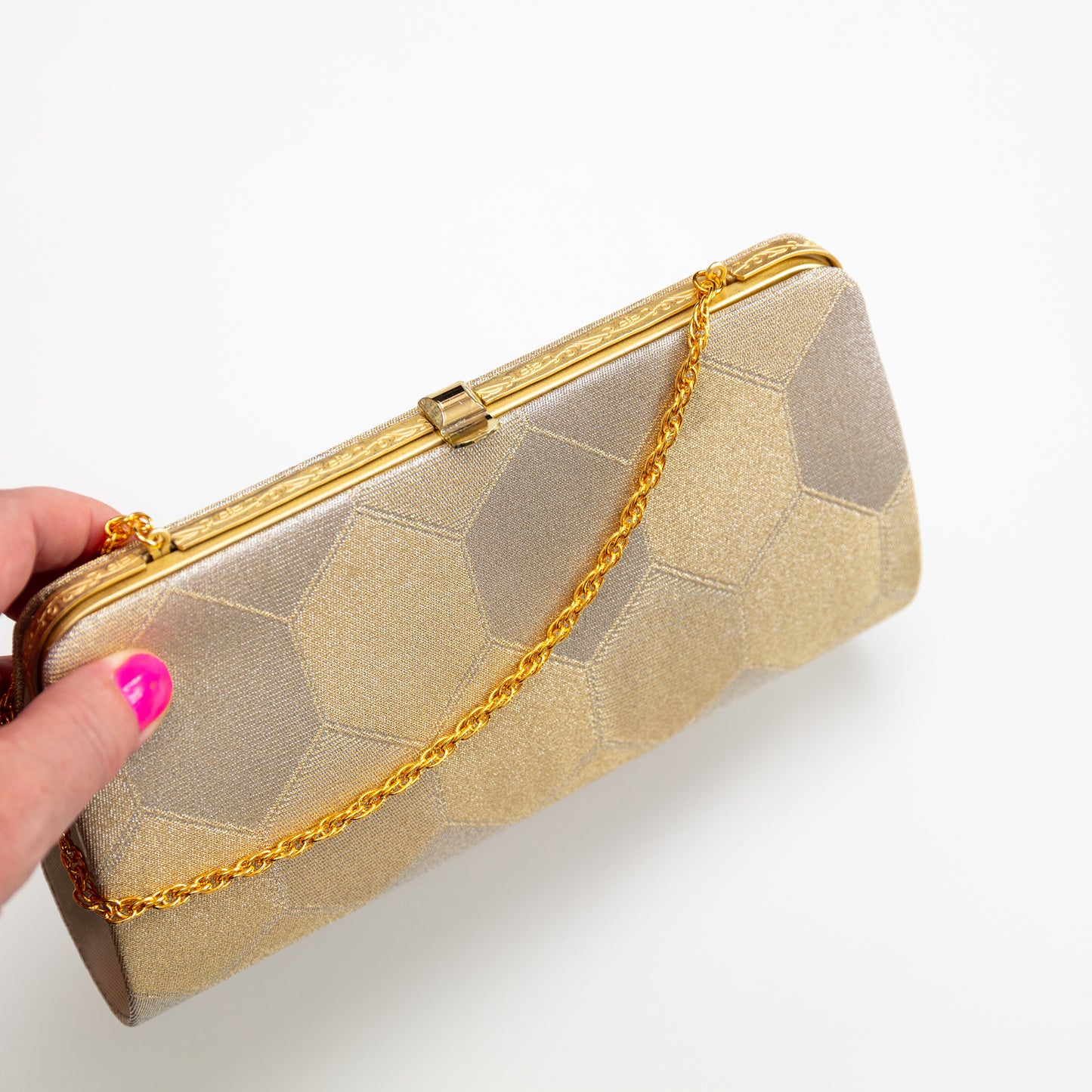 Gold clutch with chain strap held by a hand on a white background