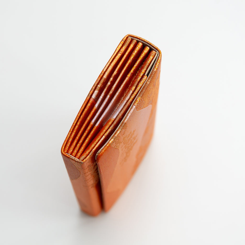 Close-up of the bronze silk envelope clutch’s intricate landscape scene embroidery and textured surface from a diagonal