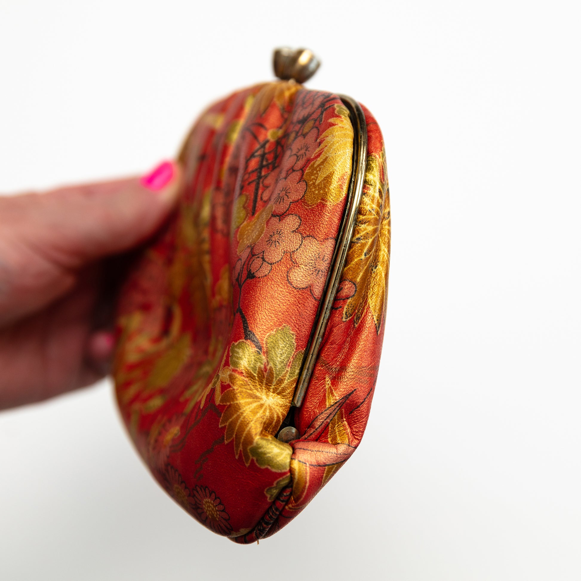 Hand holding a red and gold floral patterned clutch bag on a white background