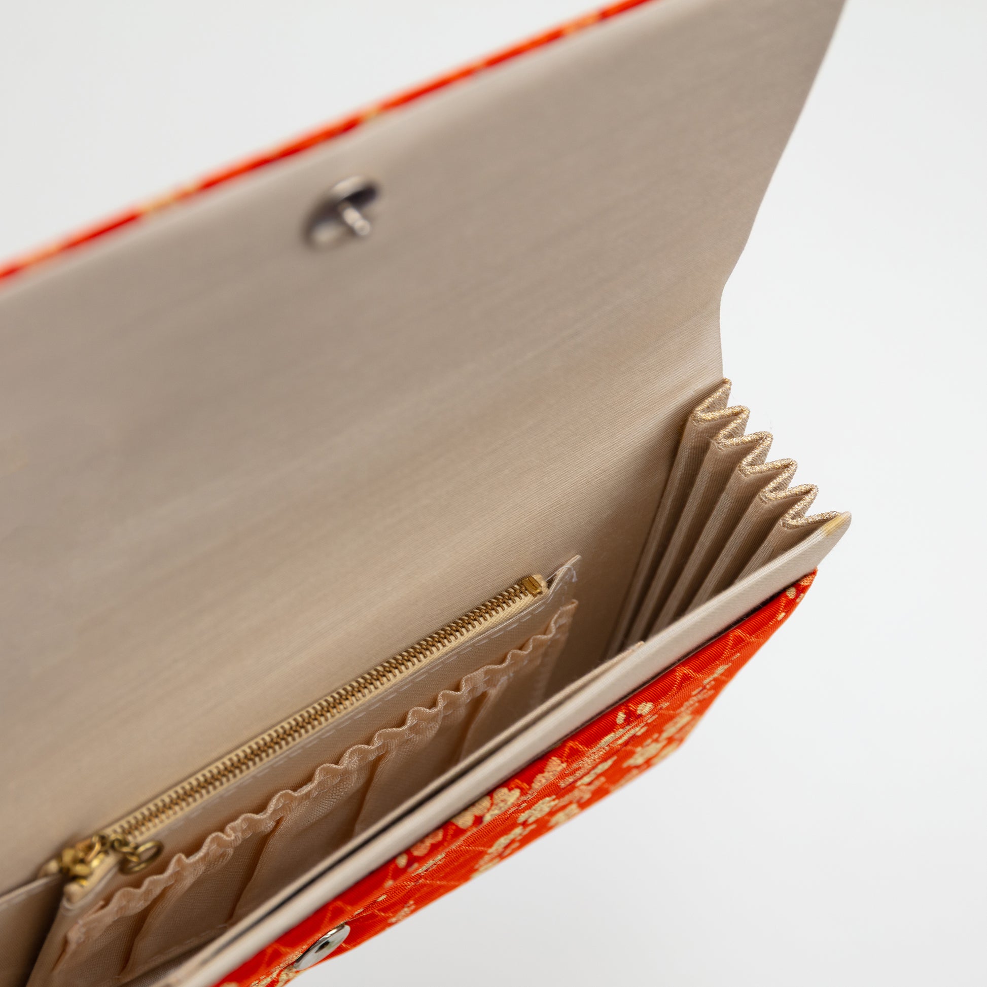 Orange silk clutch bag open to show the beige silk lining inside with zip pocket and gathered pocket on white background.