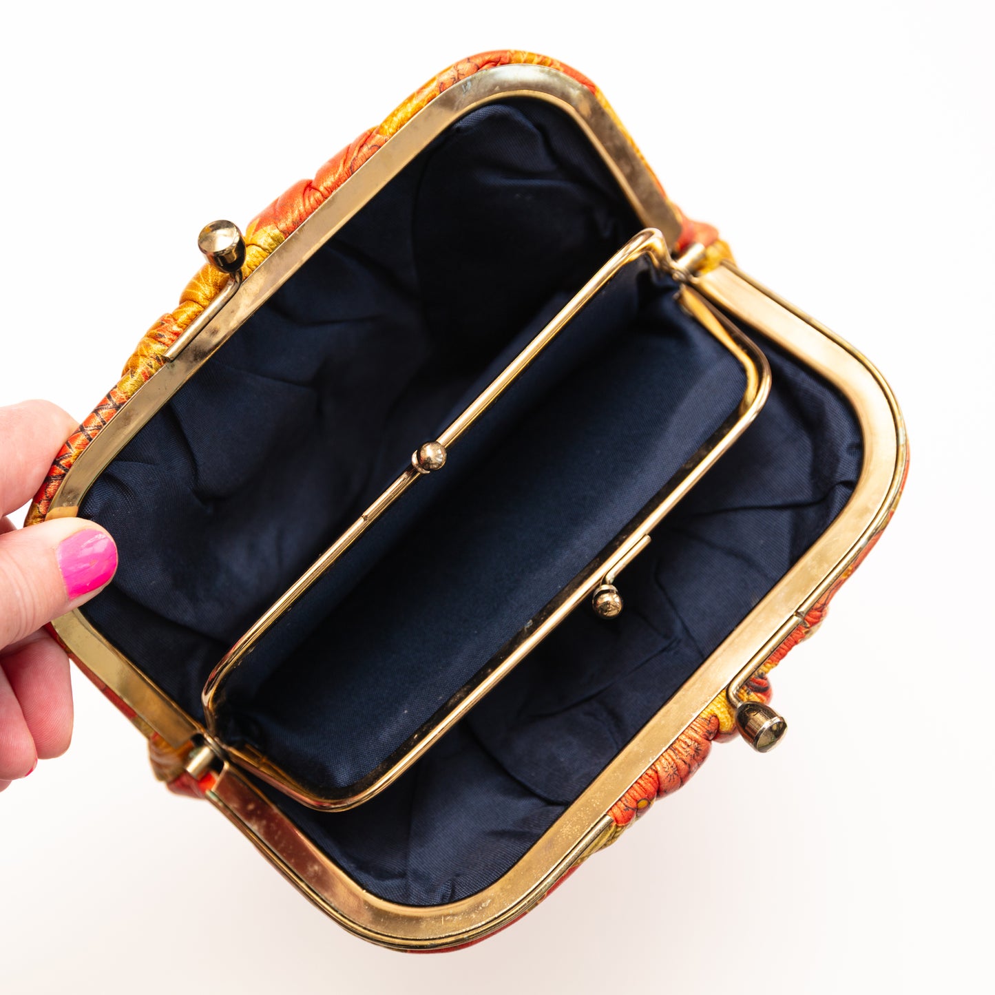 Hand holding a small clutch purse with gold frame and colorful fabric, on a white background