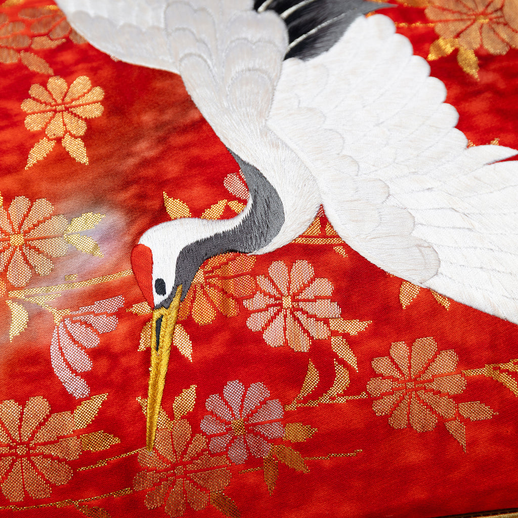 Close-up of the gold fan and crane embroidery details on the red silk bolster pillow fabric, highlighting intricate