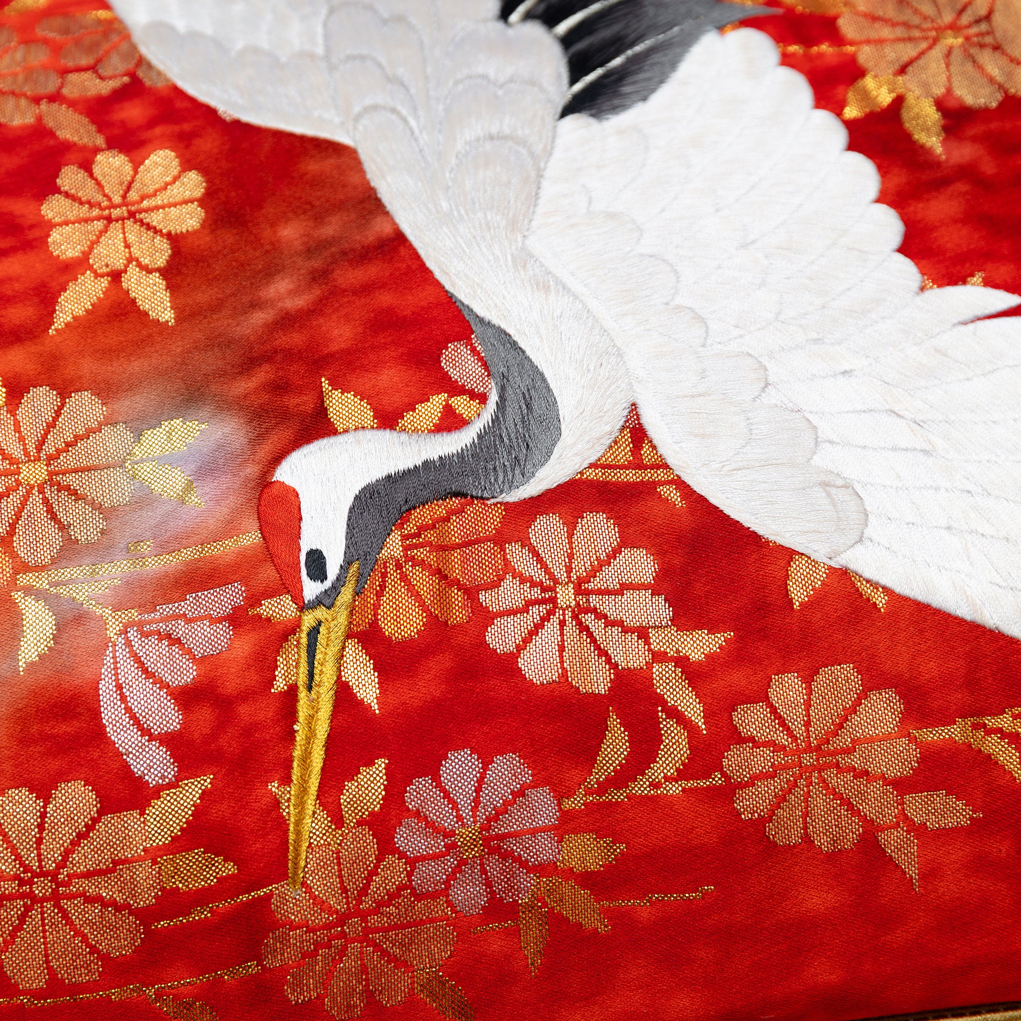 Close-up of the gold fan and crane embroidery details on the red silk bolster pillow fabric, highlighting intricate
