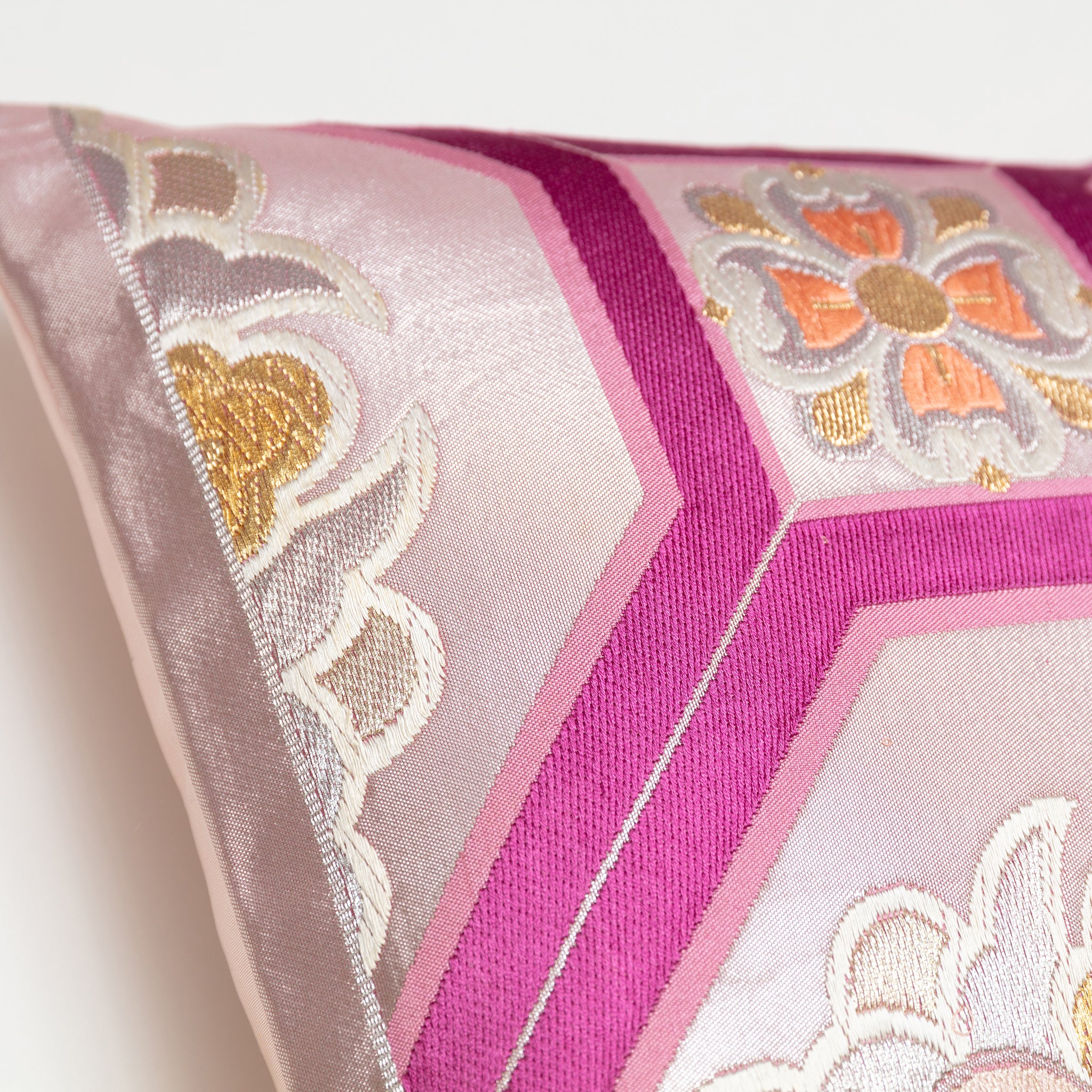 Close-up of mauve orange floral accents and textured silk fabric on the metallic pink Obi Pillow's corner detail.