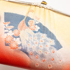 Close-up of peach silk fabric with intricate peacock feather embroidery highlighting detailed hand-stitching and rich