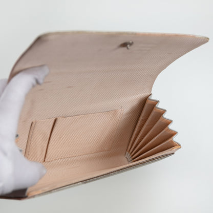 Clutch bag held open to show the interior lined in pale pink silk with internal pocket and silver closure, concertina side panels on white background.