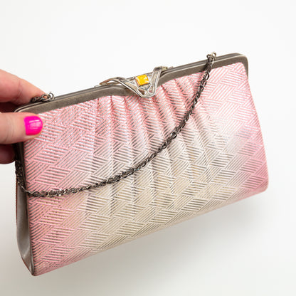 Pink and white clutch bag with a chain strap held by a hand on a white background